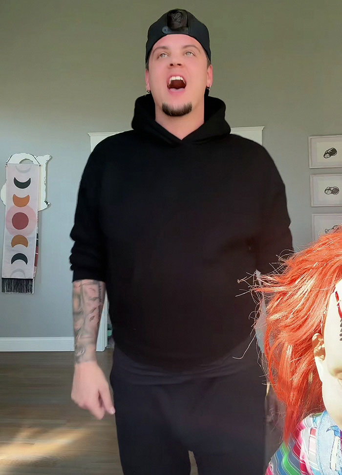 Man in black hoodie and cap standing indoors next to a doll with red hair, celebrity revealed more than they should 2025 frenzy.