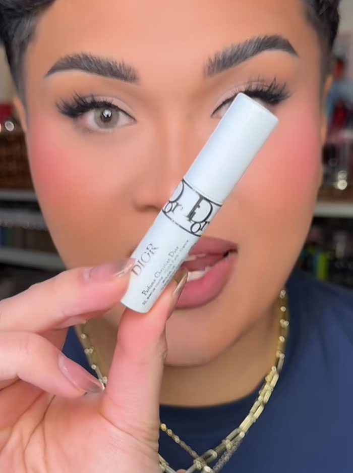 Person holding a Dior beauty product close to face, highlighting luxury brand associated with a $1,000 advent calendar controversy.