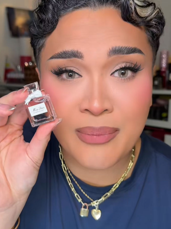 Person holding a tiny Dior perfume bottle, reacting with a puzzled expression, highlighting Dior advent calendar controversy.