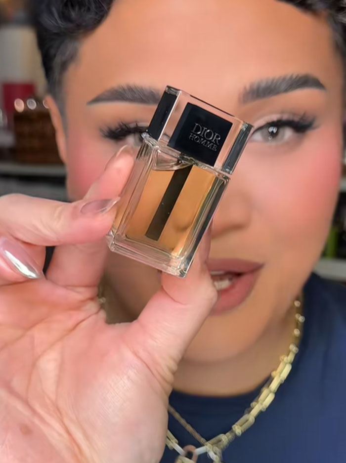 Person holding a small Dior Homme perfume bottle, highlighting luxury brand in a close-up beauty video.