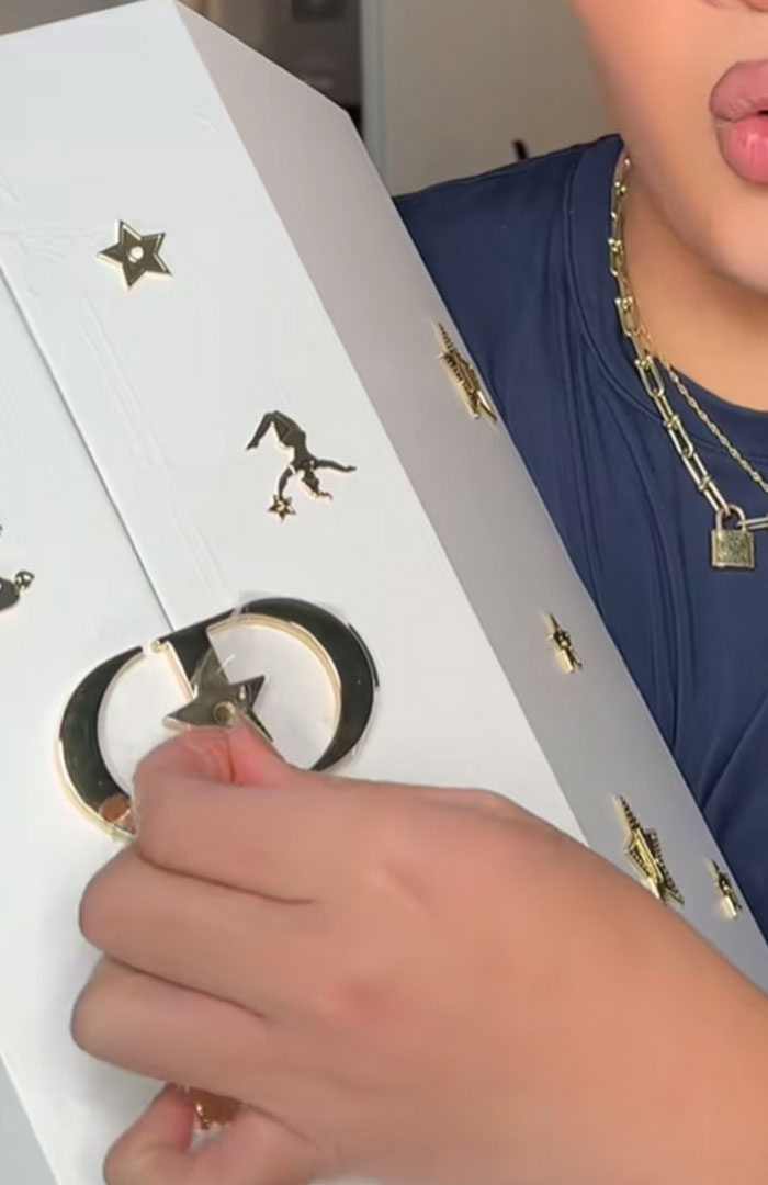 Person holding a white Dior advent calendar with gold star and crescent moon designs, showcasing luxury packaging details.