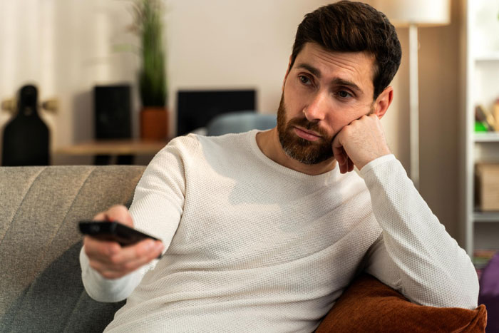 Man looking unmotivated on couch holding remote control, reflecting ungrateful husband and support parenting challenges.