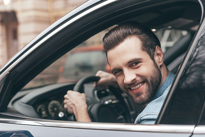 A man smiling while driving a car, representing solo female travelers feeling powerless in unsafe places.