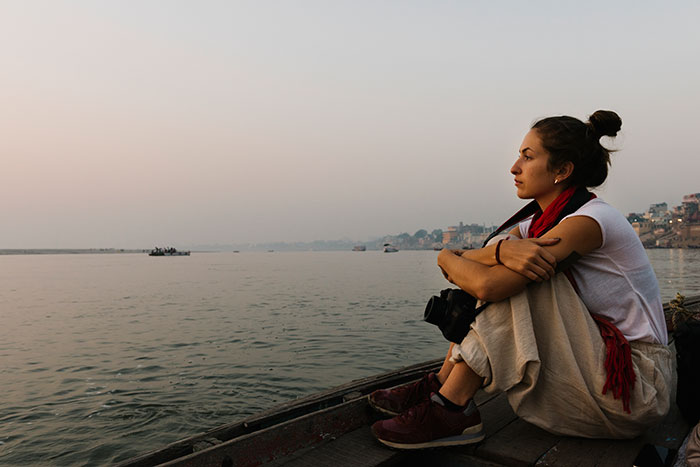 Solo female traveler sitting on a boat by the river at sunset, reflecting on challenging travel destinations.