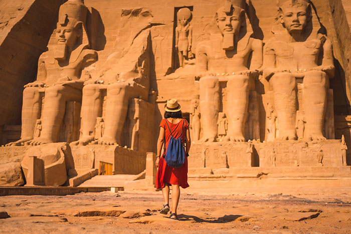 Solo female traveler in a red dress exploring ancient Egyptian statues at a historic archaeological site.