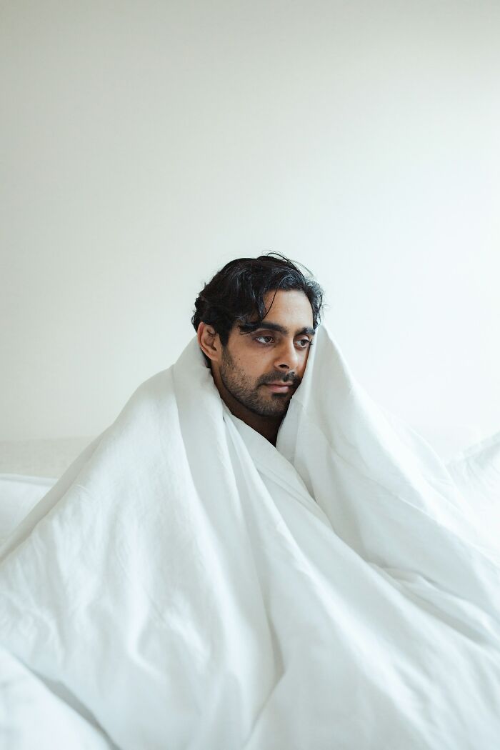 A man wrapped in a white blanket sitting on a bed, reflecting on mysterious medical issues and diagnoses.