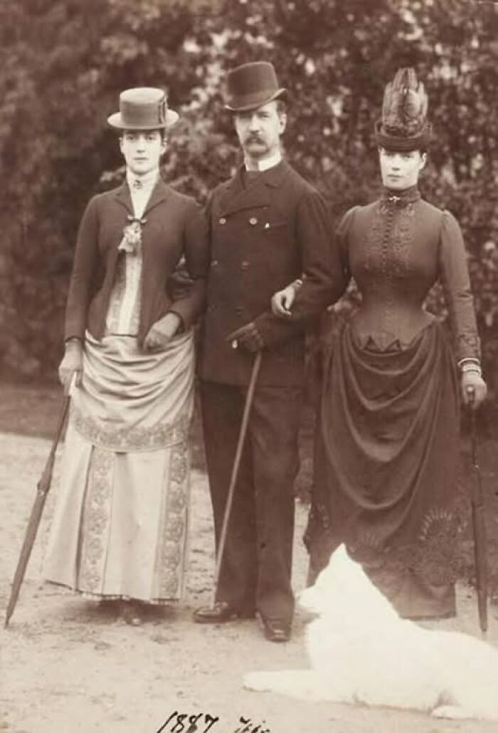 Victorian-Edwardian pictures of three people in period clothing standing outdoors with a white dog lying nearby.