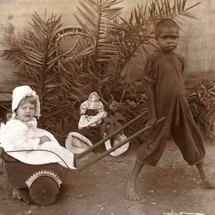 Young boy pulling a cart with a child sitting inside, vintage Victorian-Edwardian pictures in sepia tone outdoors.
