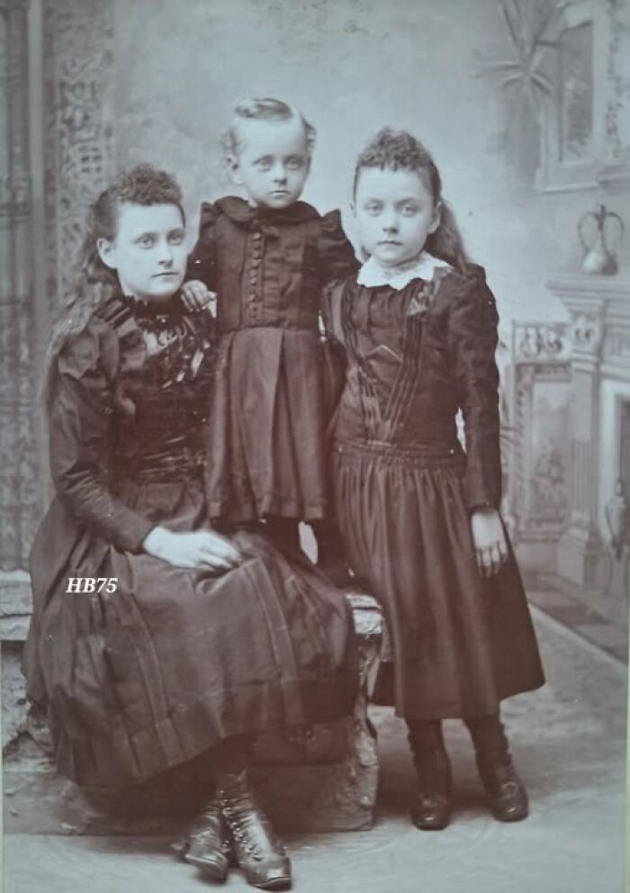 Victorian-Edwardian pictures of three children in period dresses posing in a vintage indoor studio setting.