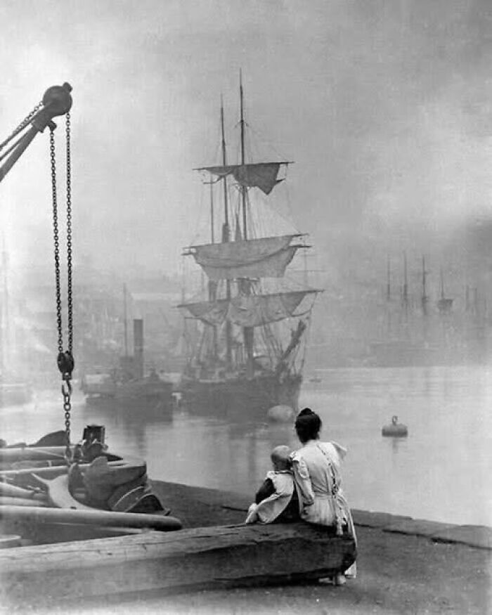 Victorian-Edwardian pictures showing a woman and child sitting by a foggy harbor with sailing ships in the background.