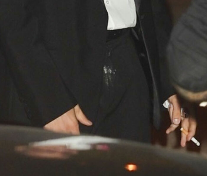 Justin Bieber in a black suit with a visible stain on his c****h area, holding a cigarette in his right hand. Justin Bieber in a black suit with a visible stain on his c****h area, holding a cigarette in his right hand.
