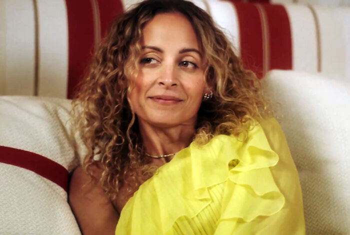 Woman with curly hair wearing a bright yellow ruffled top sitting on a couch, sharing insights as a nepo baby insider.