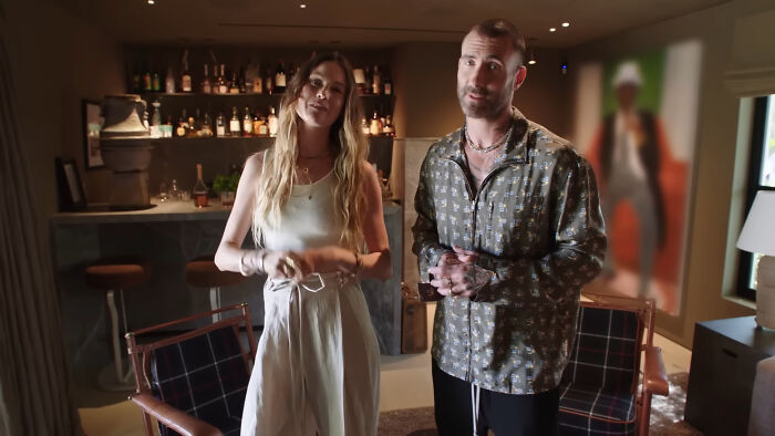 Two people standing in a dimly lit room sharing insider experiences of nepo babies in an informal setting.