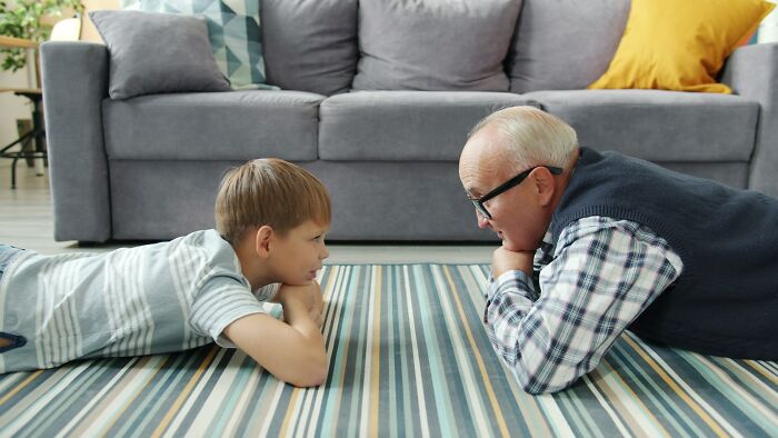 Young boy and elderly man lying on striped carpet, showing weird behavior clearly passed down from their parents.