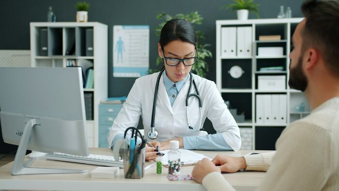 Female doctor with stethoscope talking to patient about cancer diagnosis and insensitive remarks in medical office.