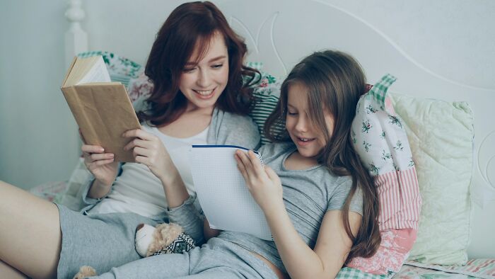 Mother and daughter sharing a cozy moment reading together, showing kids doing something weird passed down from parents.