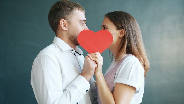 Couple holding a red paper heart between them, symbolizing trust and vulnerability in scams and their effects.