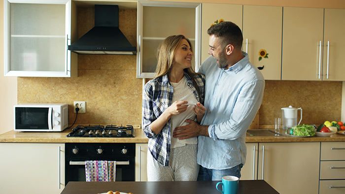 Woman smiling and talking with man in kitchen, asking about stepchildren and home or boarding school options.