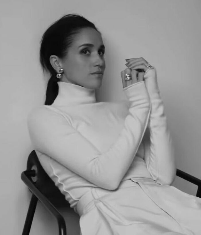 Meghan Markle in a makeup-free cover photo, captured in black and white, sitting with hands clasped and hair tied back.