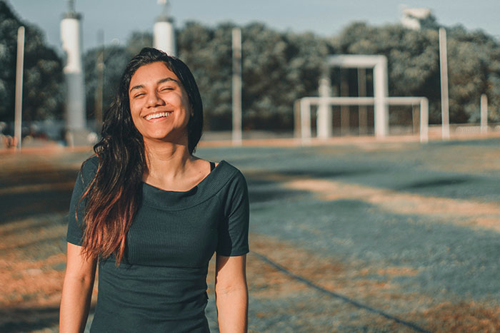Young woman smiling outdoors on a sunny day, representing an avid walker doing 20K steps per day.