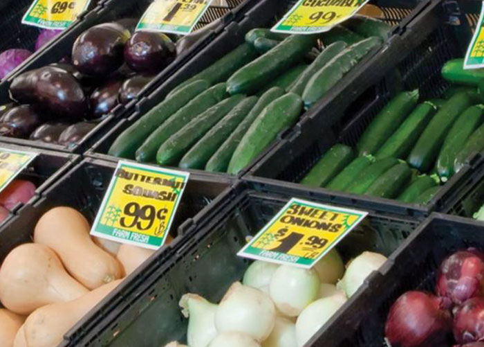 Fresh fruits and vegetables displayed in a store produce section with price tags and labels for washing tips.
