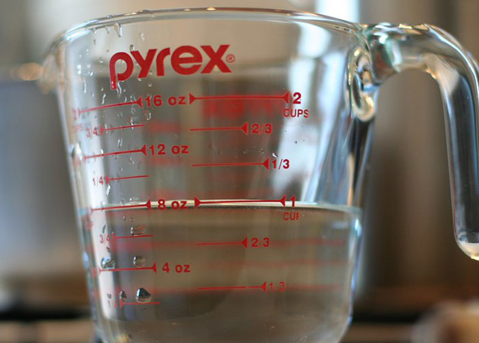Clear Pyrex measuring cup filled with water used for washing fruits and vegetables from the store.