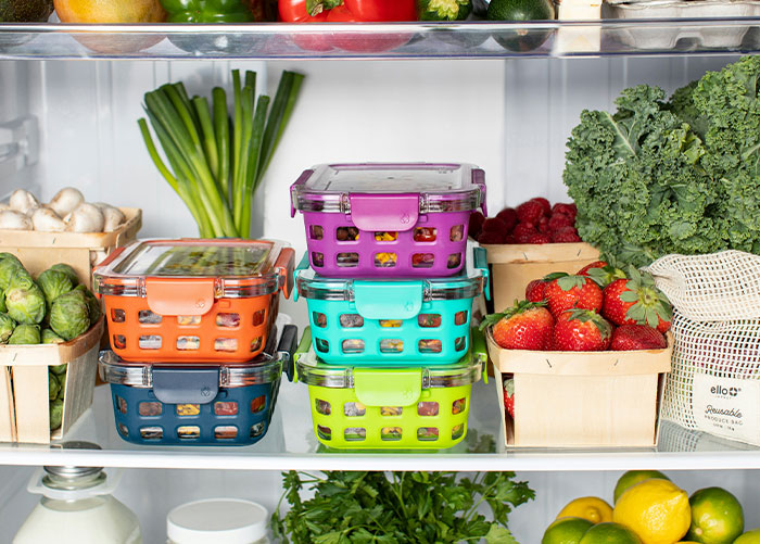 Fresh fruits and vegetables stored in colorful containers and baskets inside a clean refrigerator, ready to be washed and eaten.