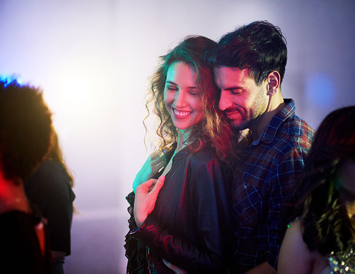 Couple enjoying a close moment at a party, illustrating dynamics between men and women in social settings.