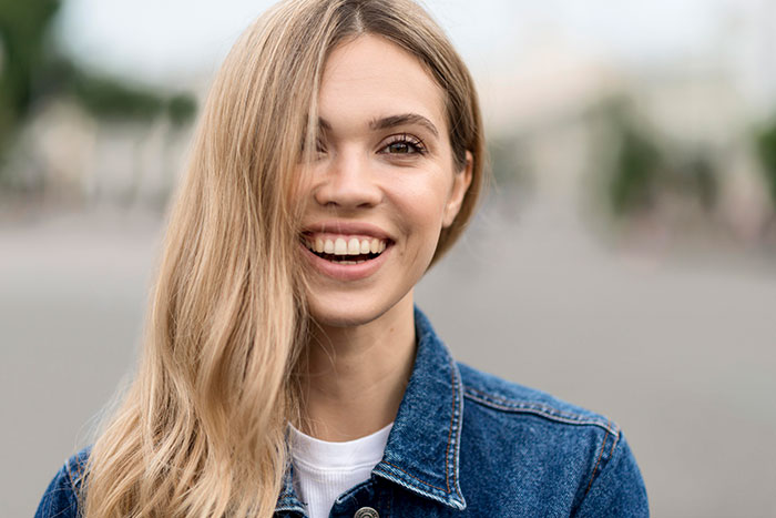 Young woman with long blonde hair and denim jacket smiling outdoors, representing men’s views on women’s unhinged behaviors.