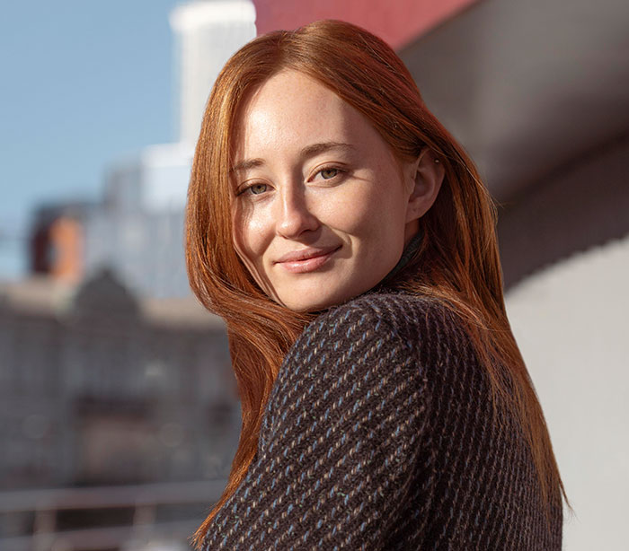 Red-haired woman smiling outdoors on a city balcony, representing women who did unhinged things men avoided.