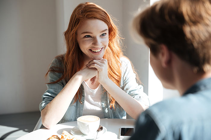 Young woman smiling and chatting with a man over coffee in a bright cafe setting, showing connection and conversation.