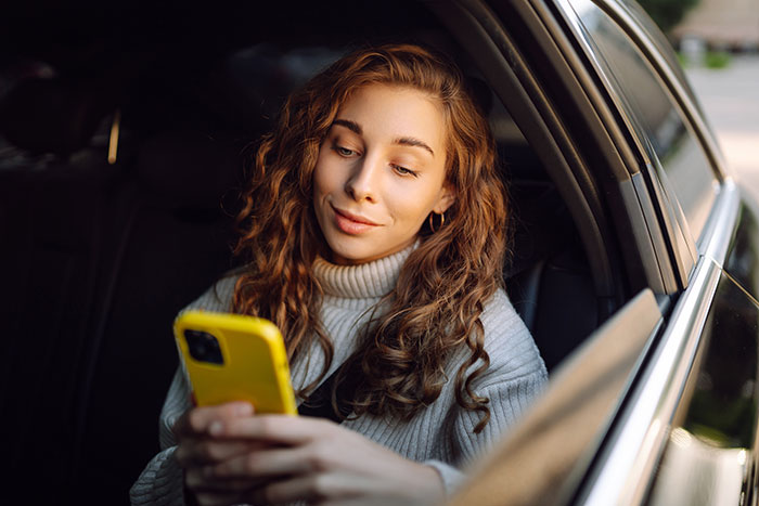 Young woman with curly hair sitting in a car looking at her phone, reflecting on things men didn’t want to share with women.