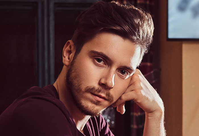 Young man with beard resting his head on hand, looking thoughtful, reflecting on men and unhinged behaviors of women.