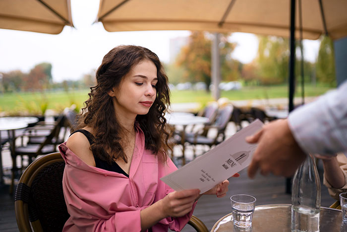 Woman reading a menu at an outdoor café, representing women who did unhinged things men didn’t want in common with.