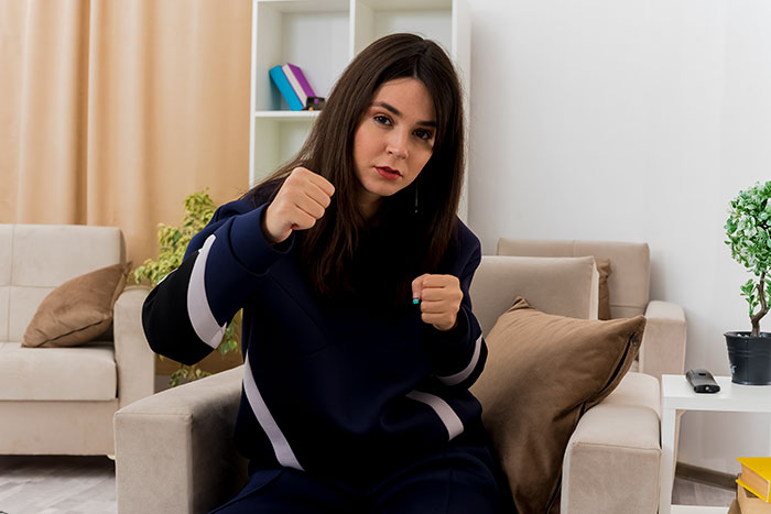 Young woman sitting on a couch with fists raised, illustrating unhinged behavior men want to avoid in women relationships.