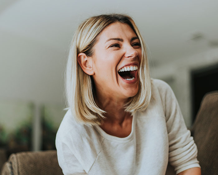 Woman with blonde hair laughing joyfully indoors, depicting unhinged behavior men didn’t want to have in common.