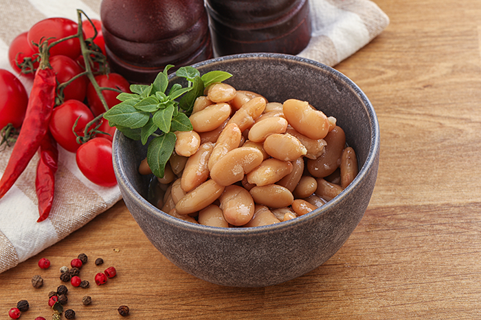 Bowl of beans on wooden table with chili peppers and herbs symbolizing forbidden foods and paganism conflict.