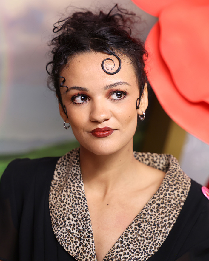 Actress with curled hair and leopard print collar reacting to Wicked cast selfie controversy on disability inclusion.