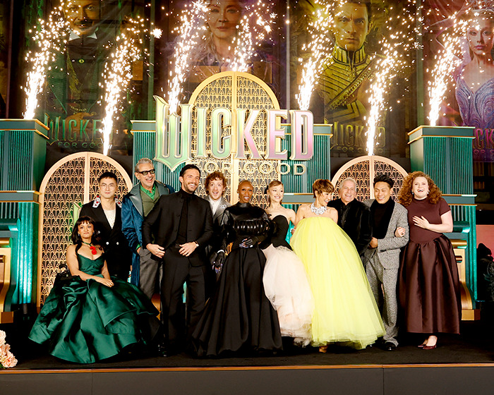 Wicked cast posing on stage with fireworks during event, sparking debate on disability inclusion and exclusion issues.