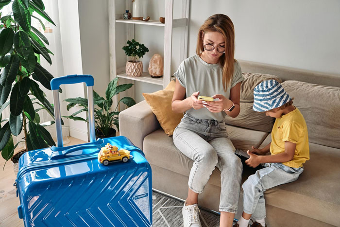 Mother and child at home with blue suitcase, preparing for family vacation amid husband&rsquo;s business priorities conflict.