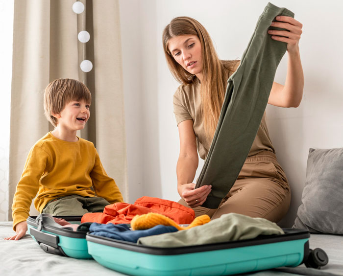 Mother packing clothes in suitcase while her son watches, illustrating family vacation planning and travel priorities conflict.