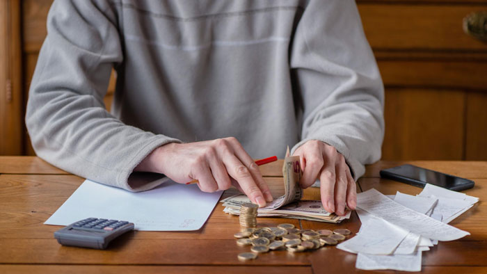Man counting money and coins at a table with receipts and a calculator, illustrating financial support for in-laws.