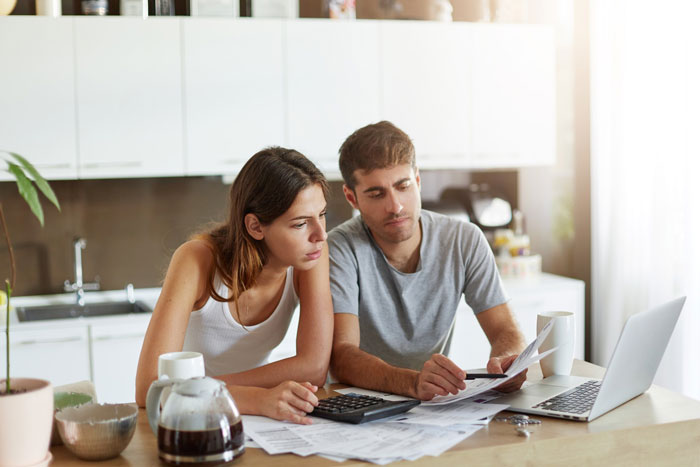 Couple reviewing bills and financial documents at kitchen table, stressed about in-laws and family support issues.