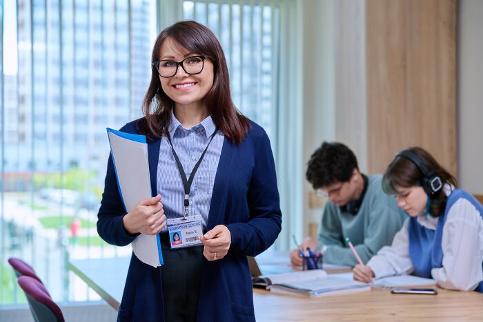 Smiling woman with glasses holding documents in a bright office, representing cancer insensitivity awareness and support.