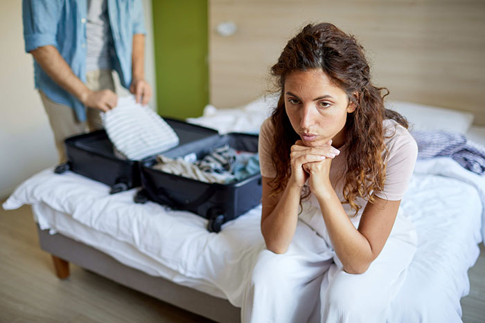Woman looks worried as man packs suitcase for suspicious work trip, triggering relationship doubts and tension in the room.