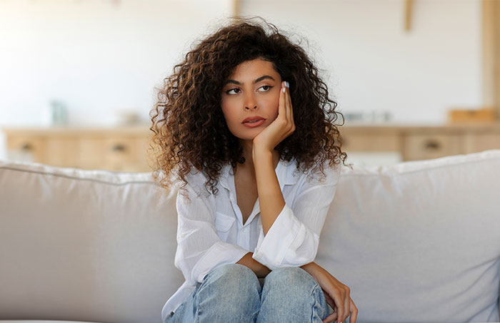 Young woman sitting on couch looking upset and thoughtful about guy secretly giving his sister a key to GF&rsquo;s house