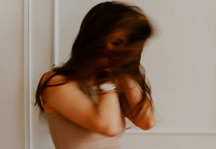 Young woman in motion with blurred hair, expressing emotion in a soft neutral background, woman child concept image.