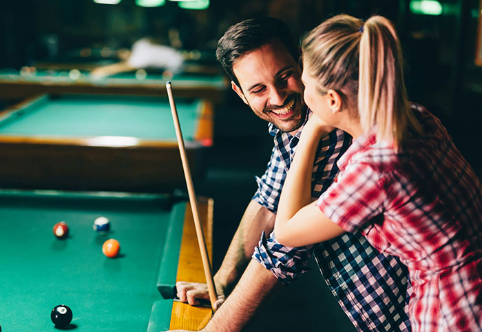 A playful woman and man smiling by a pool table, capturing the spirit of a woman child enjoying fun moments.