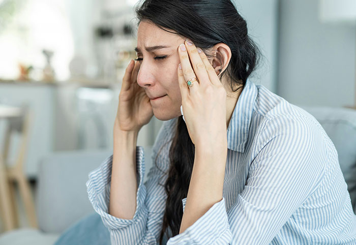 Young woman experiencing stress and frustration, holding her head with both hands in a casual home setting.