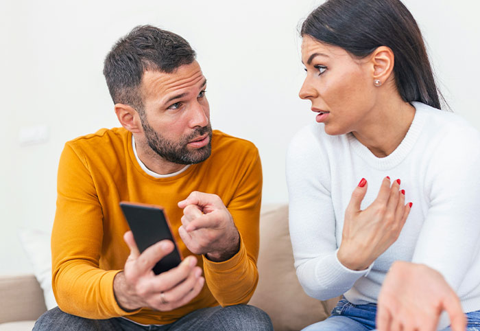 Man and woman in a heated discussion on a couch, illustrating signs of woman child behavior in relationships.